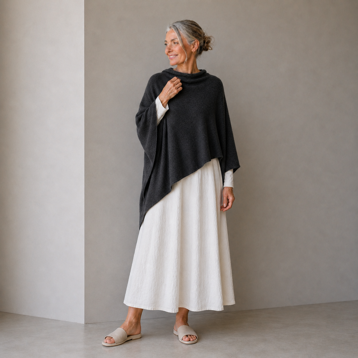 Woman wearing a black poncho over a white dress against a plain background