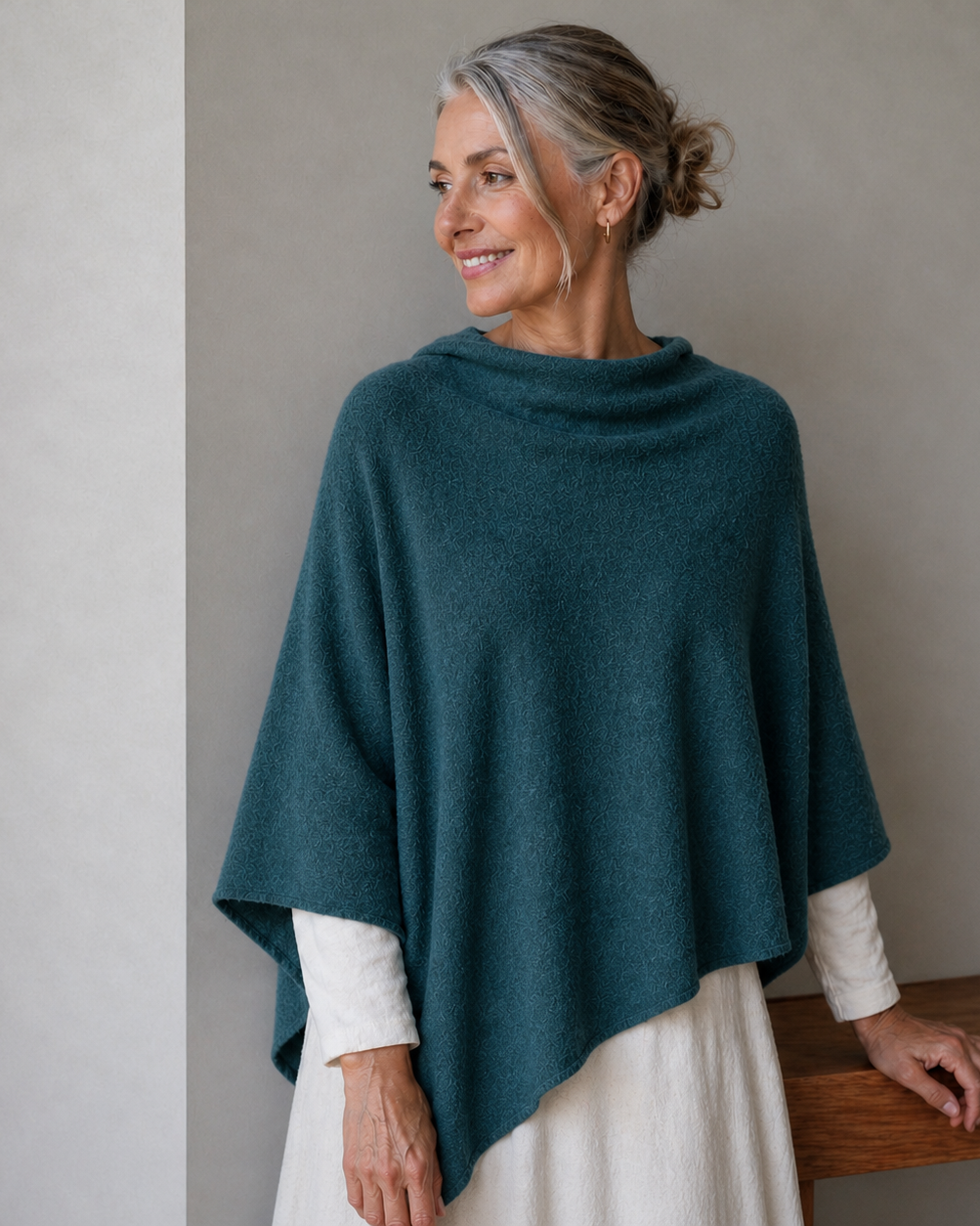 Woman wearing a teal poncho over a white dress, standing against a plain background