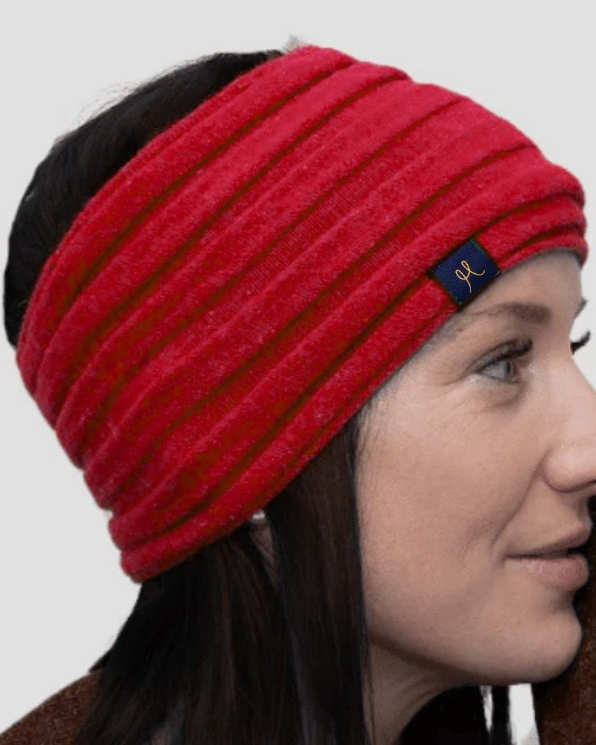Woman wearing a red knitted headband with a brand logo on a plain background