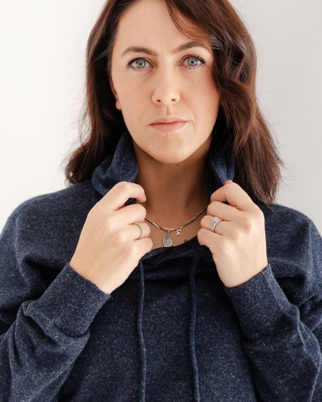 Woman adjusting the collar of a dark blue sweater against a neutral background