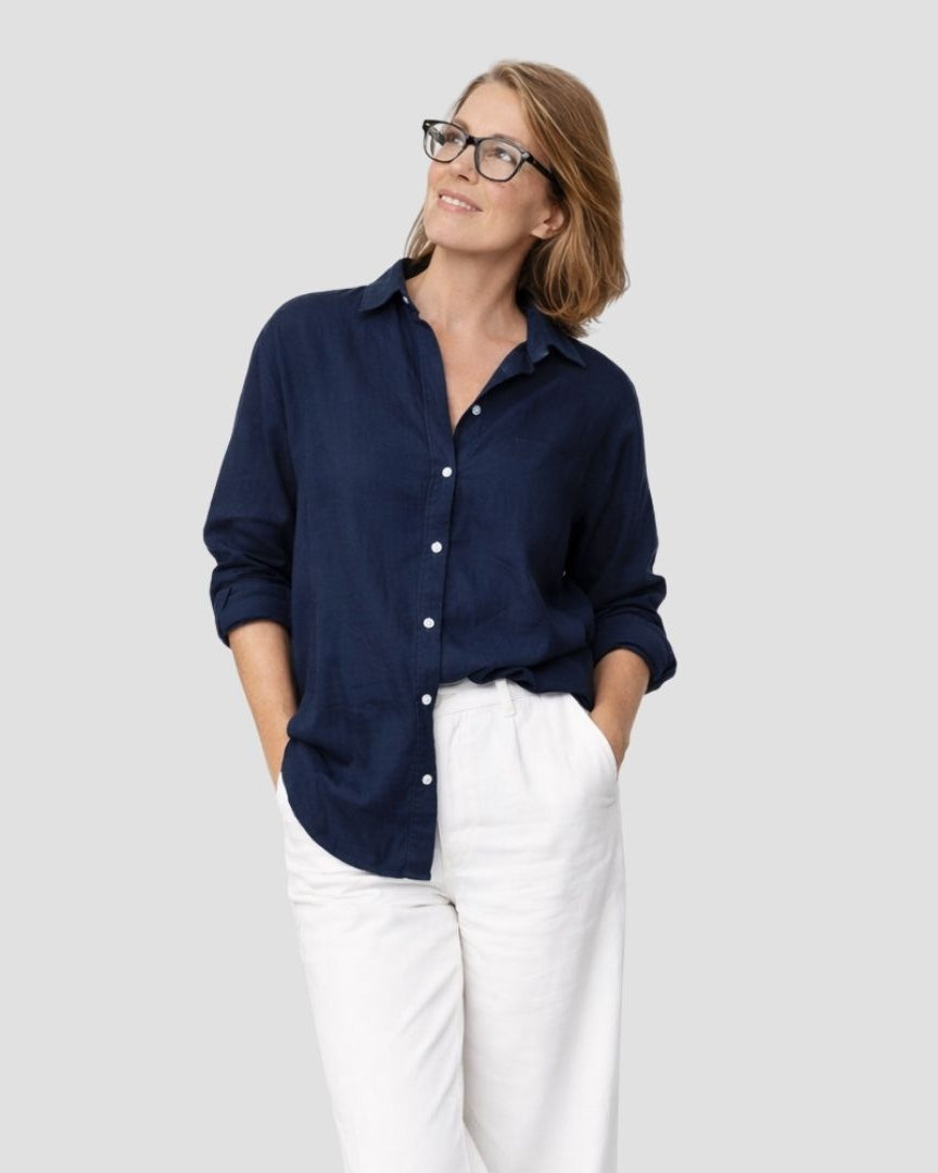 Woman wearing a navy blue shirt and white pants on a plain background