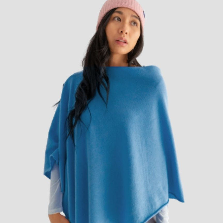 Woman wearing a blue poncho and pink beanie on a light gray background