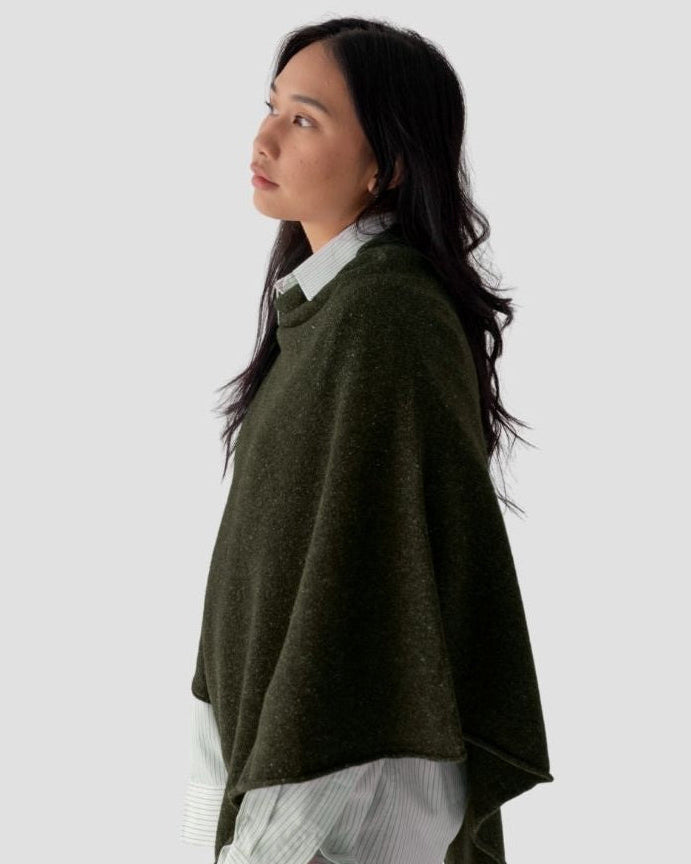 Woman wearing a green poncho over a white shirt on a light gray background