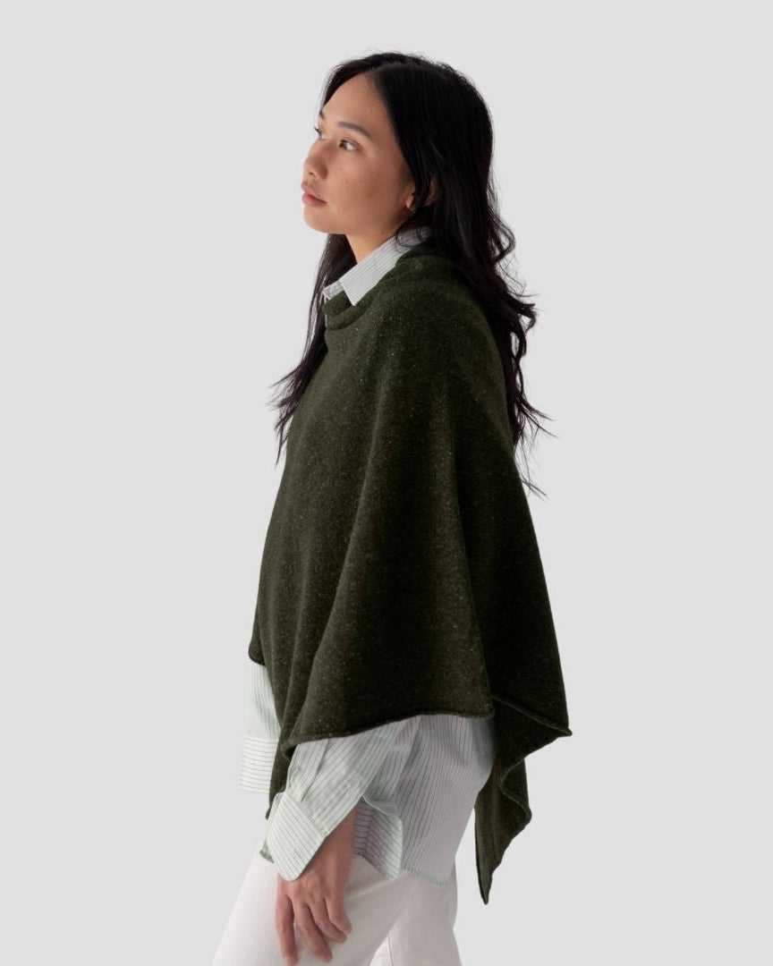 Woman wearing a green poncho over a white shirt on a light gray background