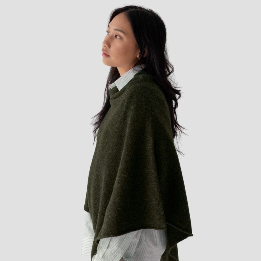 Woman wearing a green poncho over a white shirt on a light gray background