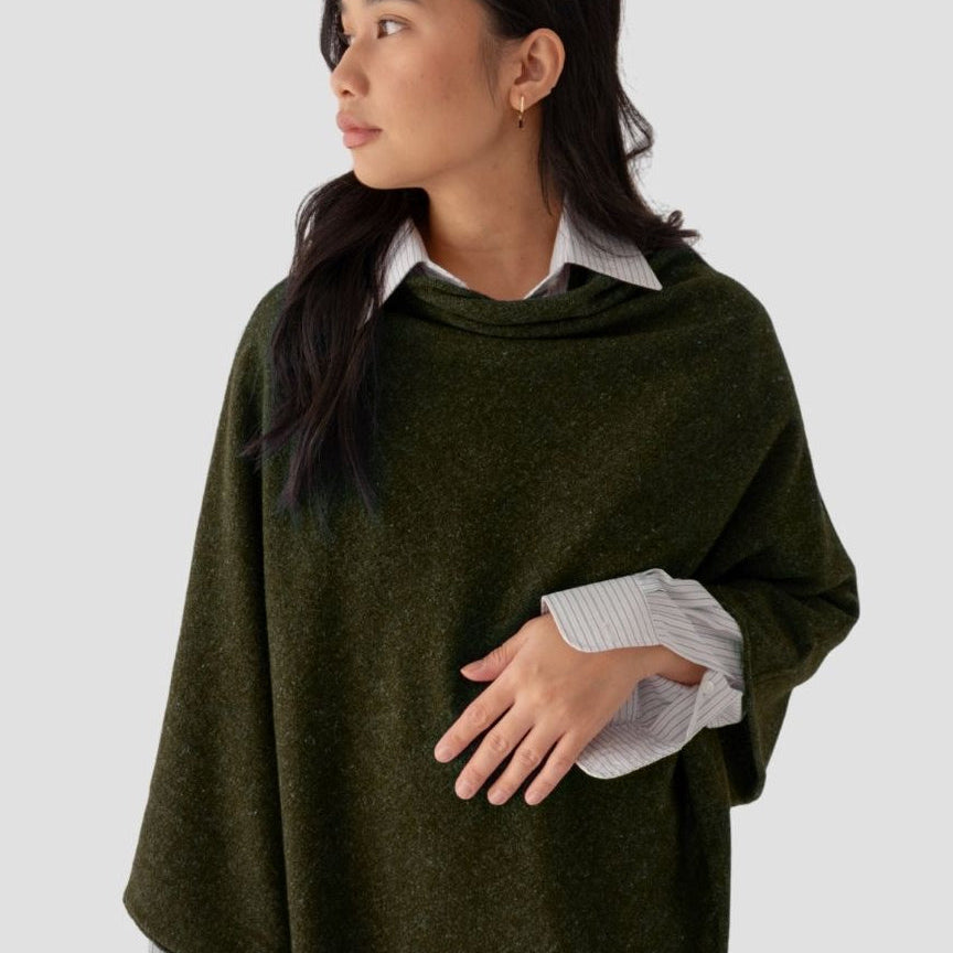 Woman wearing a green poncho over a white shirt on a light gray background
