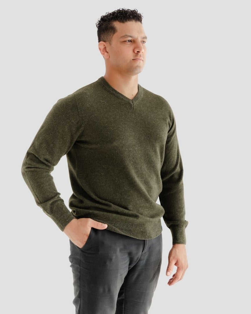 Man wearing a green sweater and dark pants against a light gray background