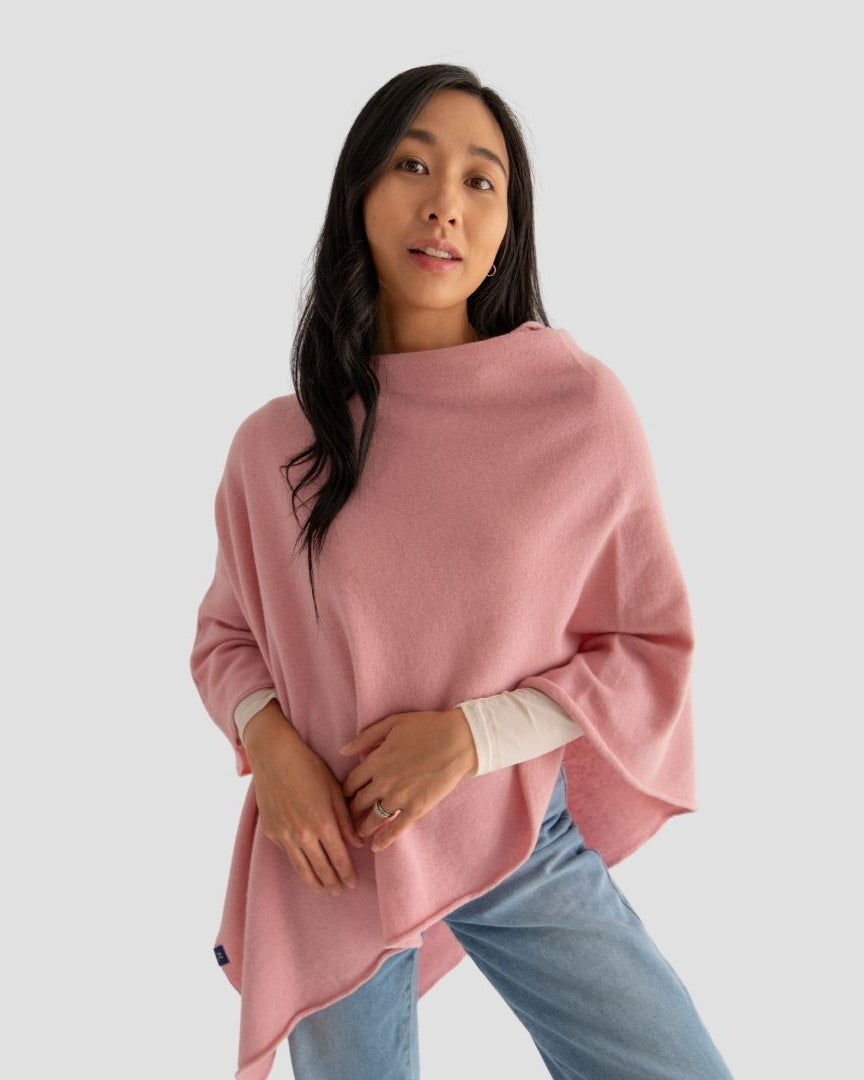 Woman wearing a pink poncho over a white shirt with light blue jeans on a plain background