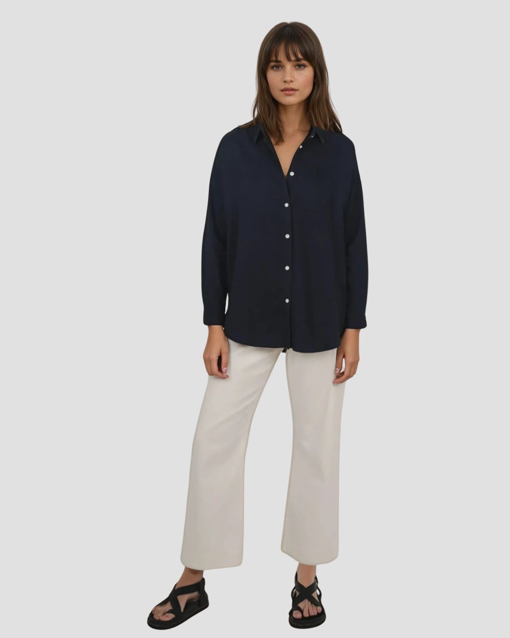 Woman wearing a navy shirt and white pants on a light gray background