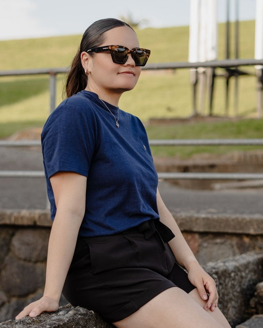 Person wearing sunglasses and a blue shirt sitting on stone steps outdoors.
