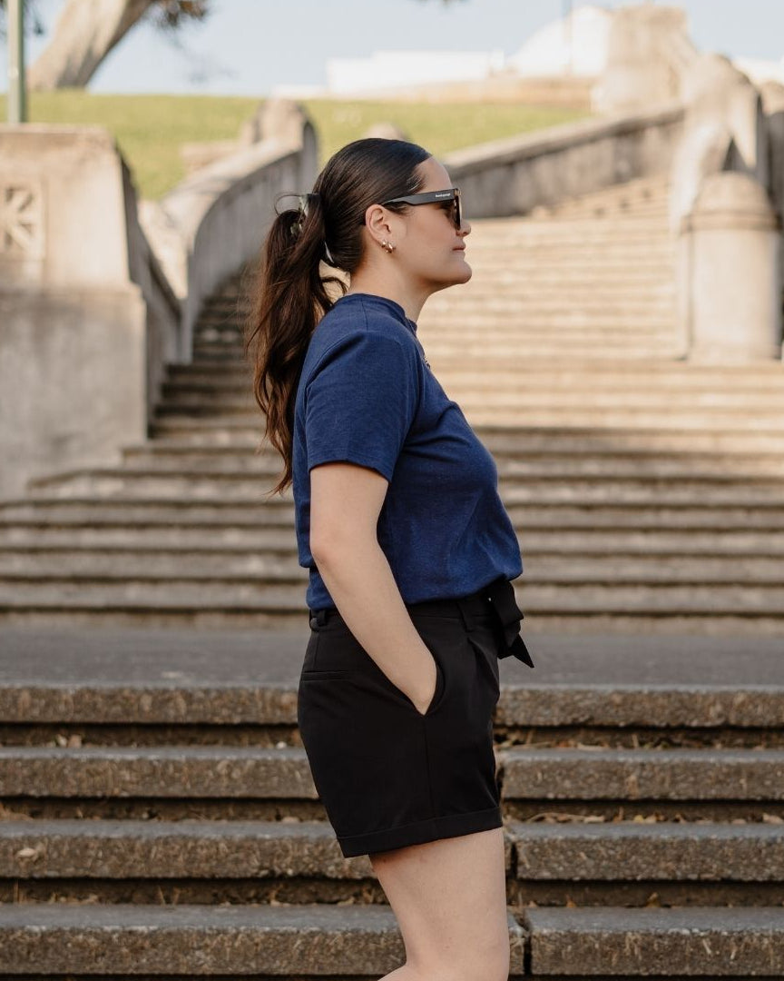 Woman in a blue shirt and black shorts standing on stone steps with a scenic background