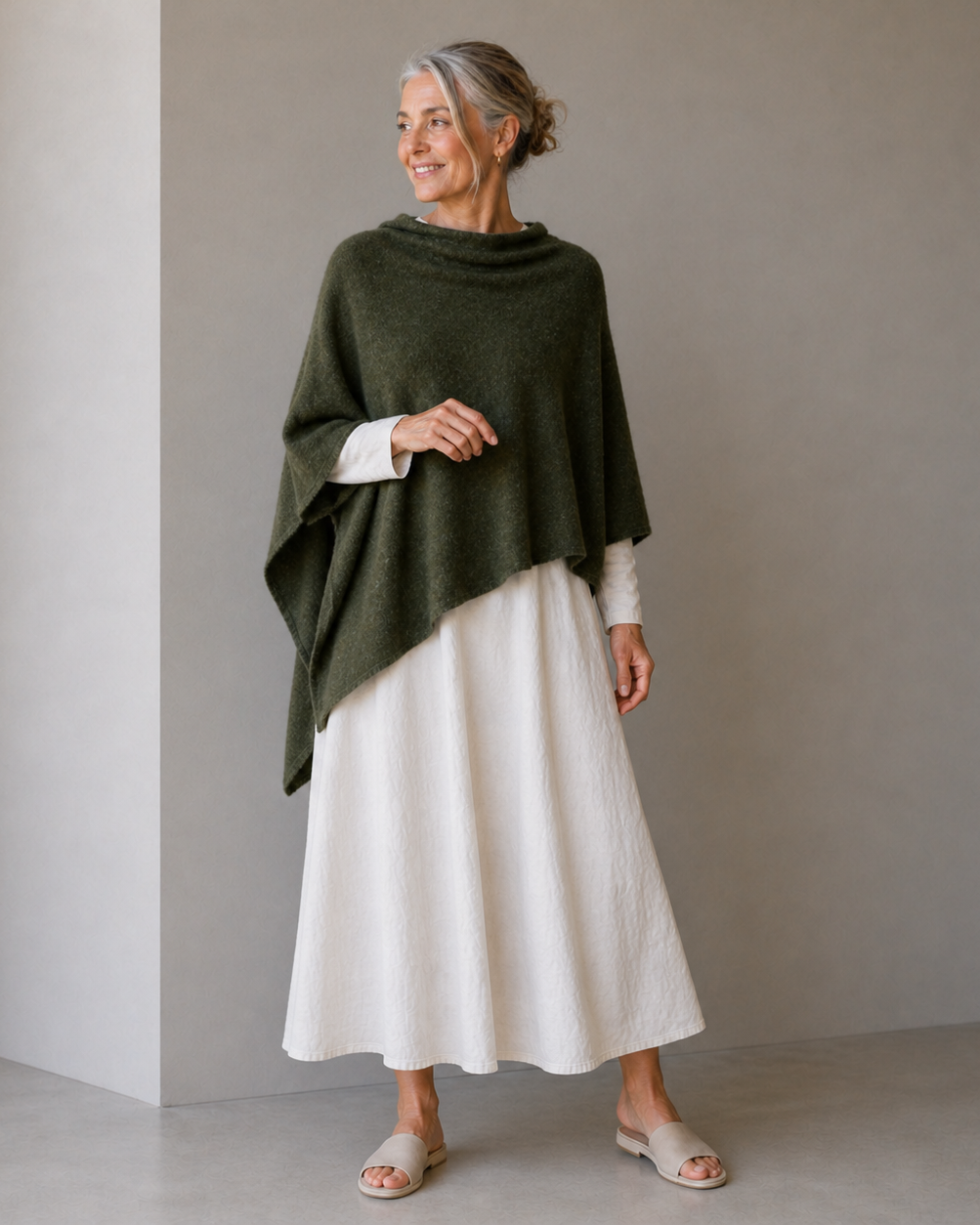 Woman wearing a green poncho over a white dress against a plain background