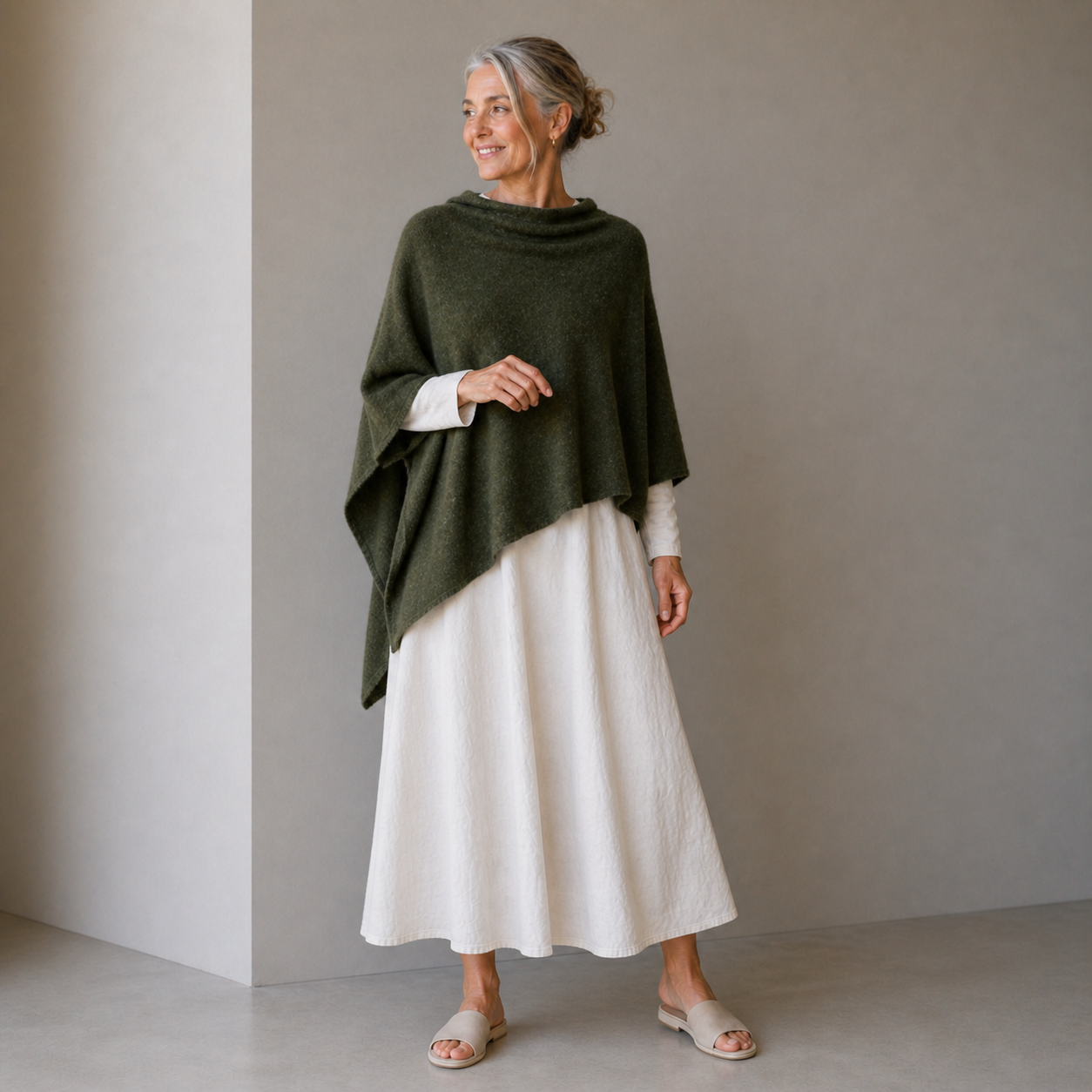 Woman wearing a green poncho over a white dress against a plain background