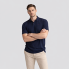 Man wearing a navy blue polo shirt and beige pants on a light gray background