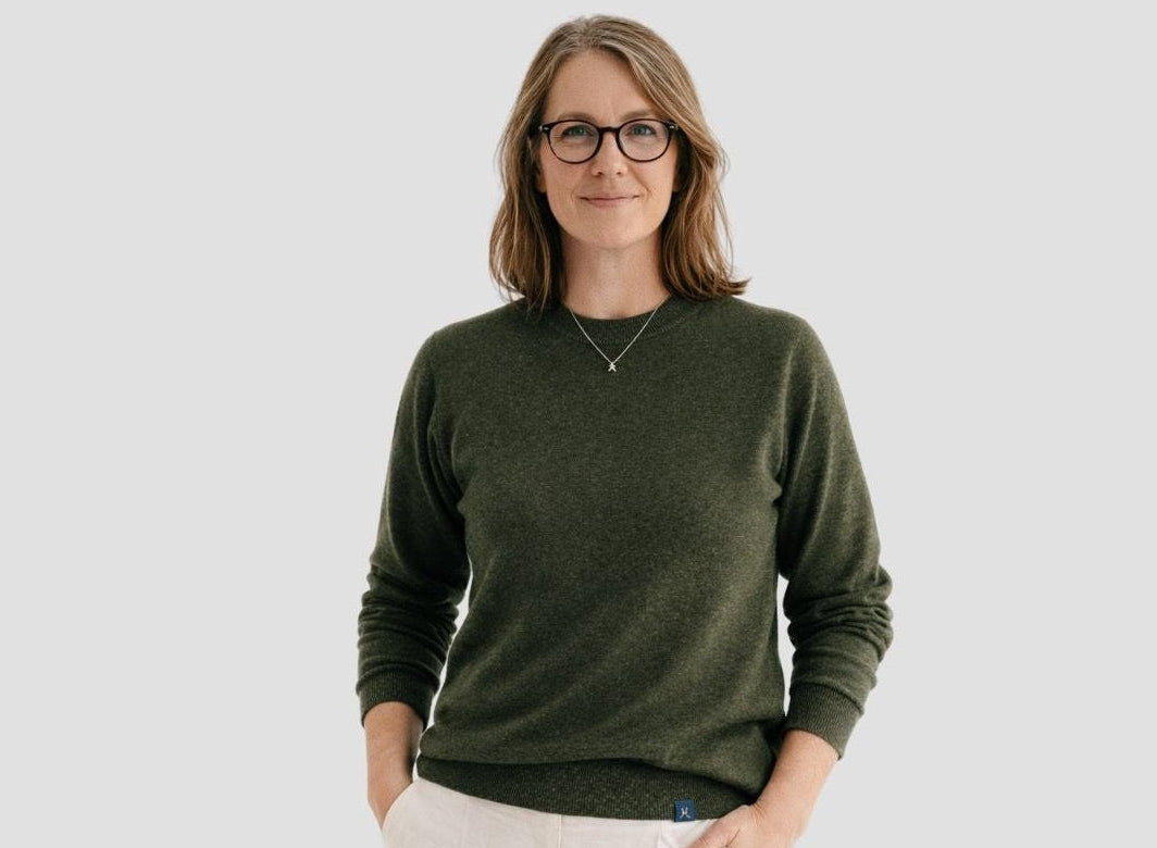 Woman wearing a green sweater and white pants against a plain background