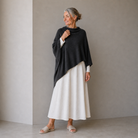 Woman wearing a black poncho over a white dress against a plain background