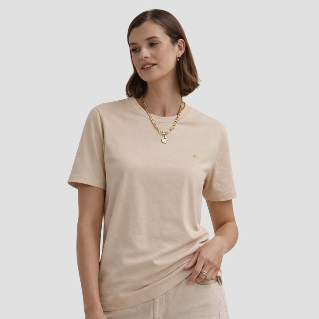 Woman wearing a beige t-shirt and gold necklace on a plain background