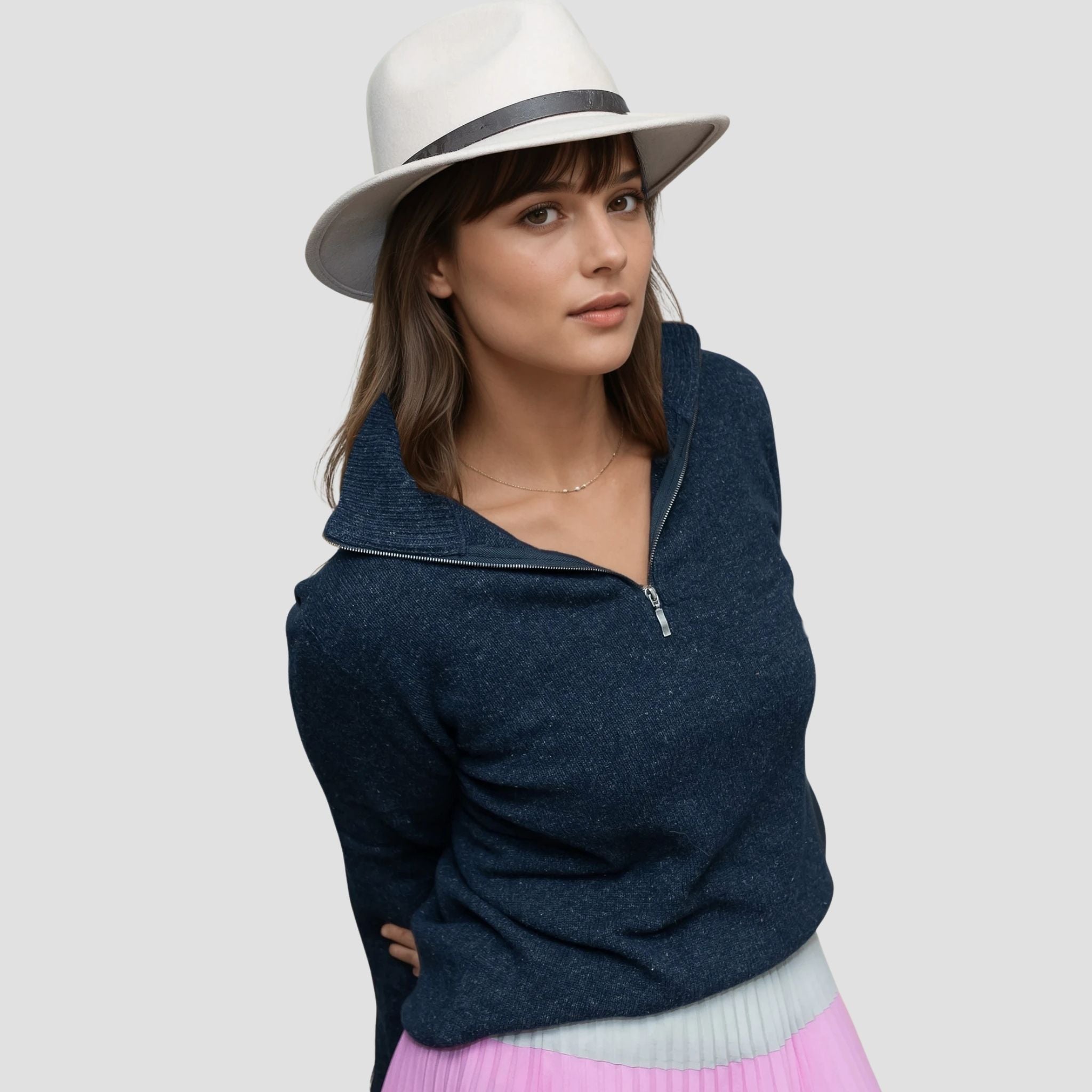 Woman wearing a navy sweater and white hat on a light gray background