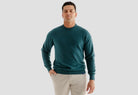 Man wearing a teal sweater and beige pants on a light gray background