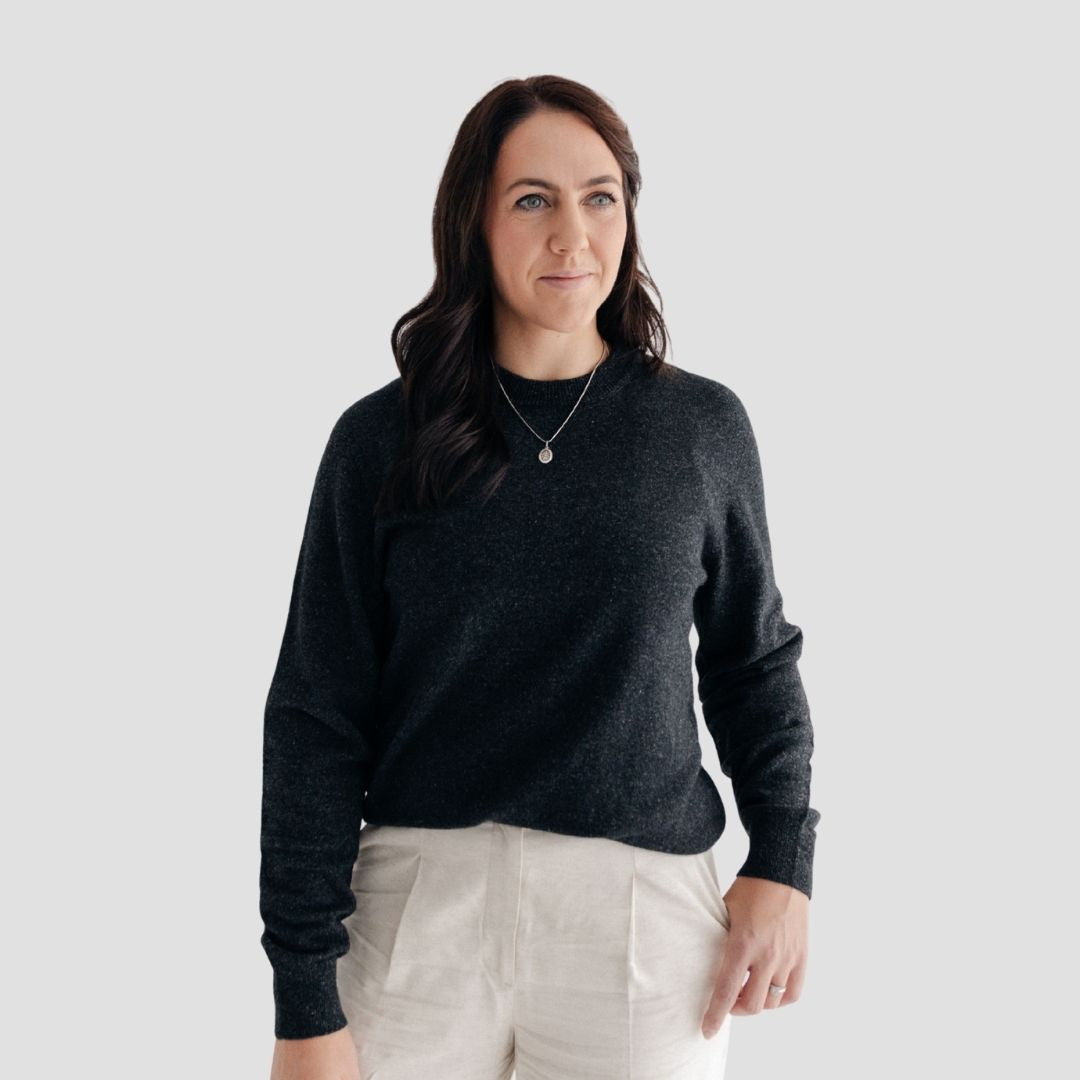 Woman wearing a dark gray sweater and light-colored pants against a plain background