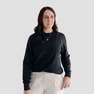 Woman wearing a dark gray sweater and light-colored pants against a plain background