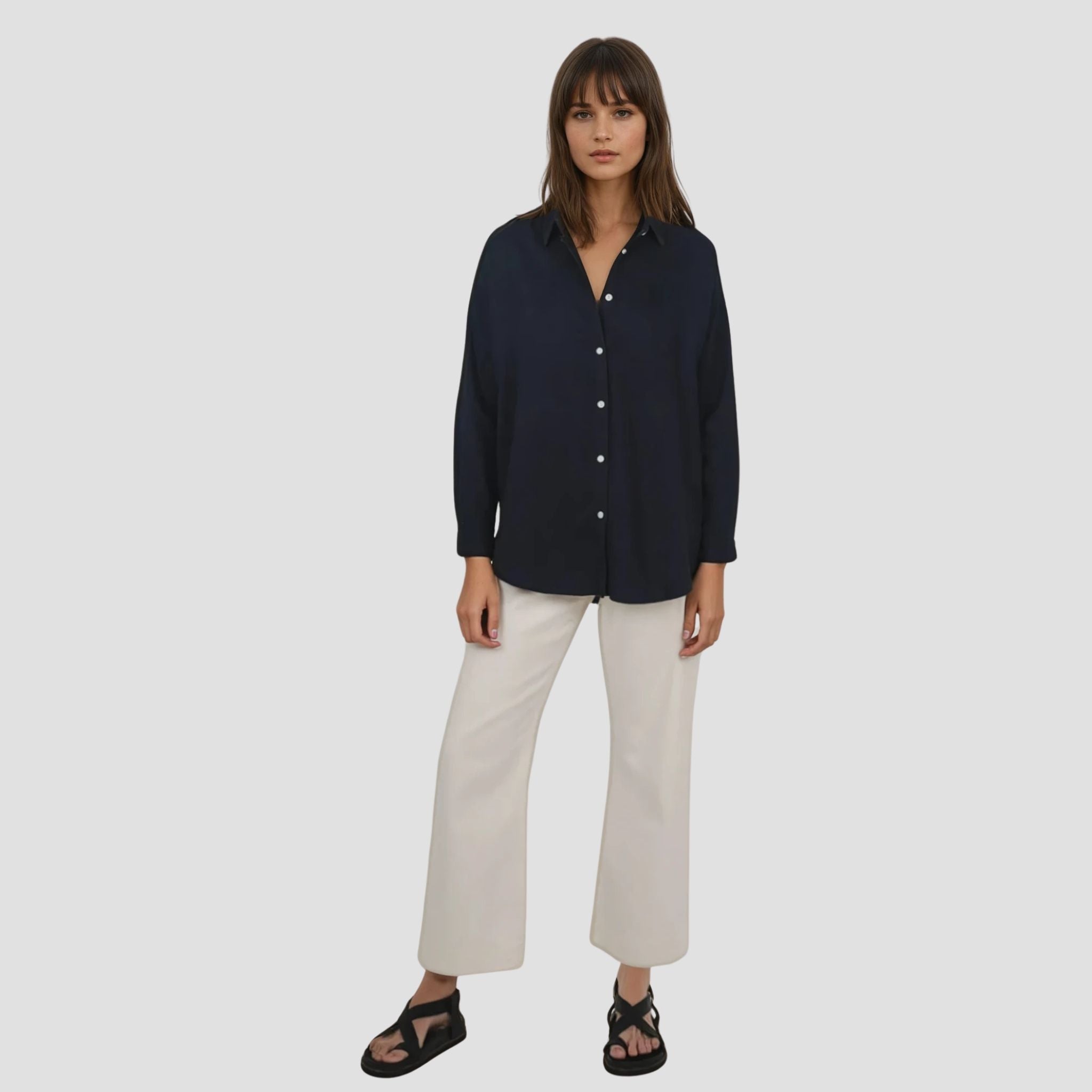 Woman wearing a navy shirt and white pants on a light gray background