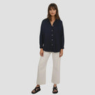 Woman wearing a navy shirt and white pants on a light gray background