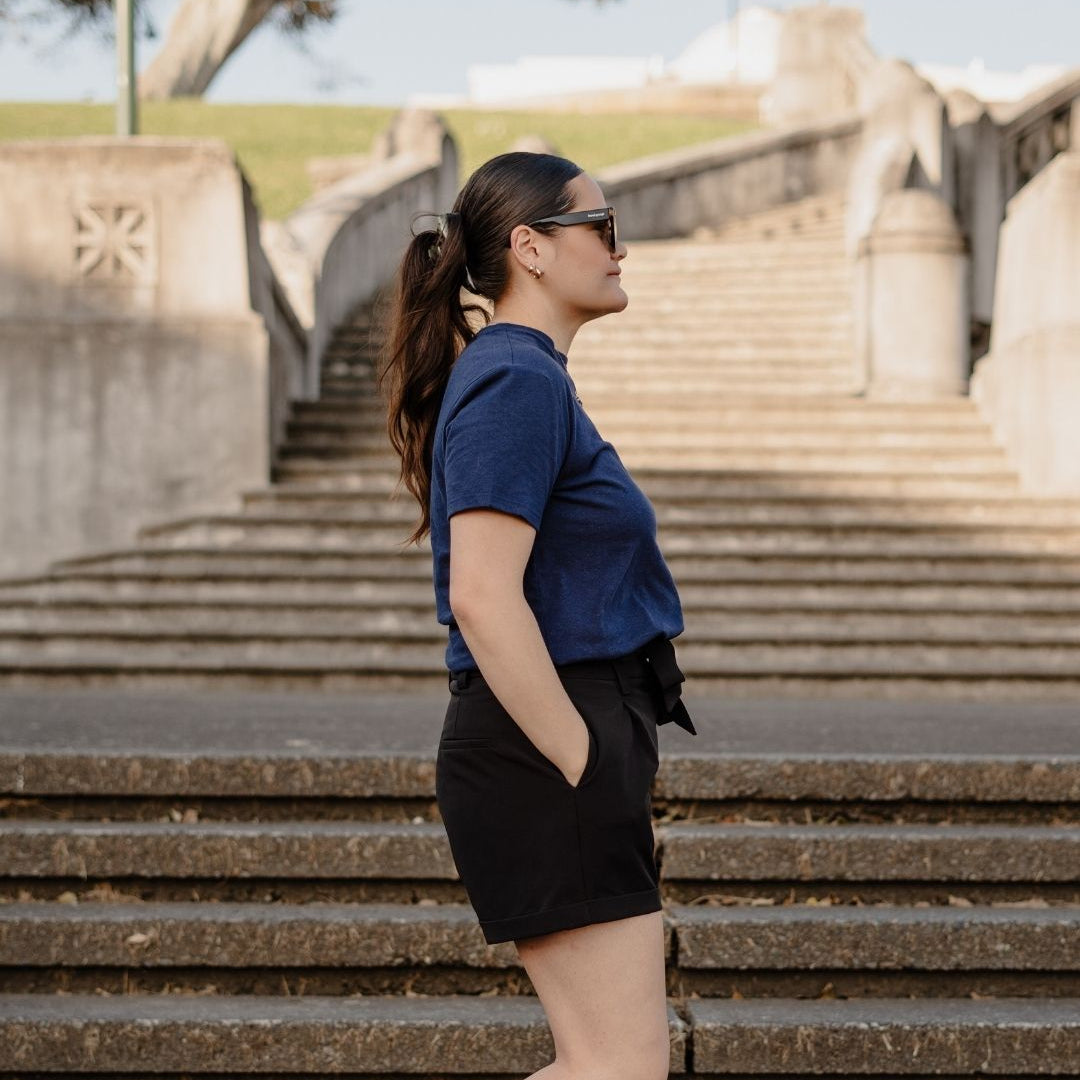 Woman in a blue shirt and black shorts standing on stone steps with a scenic background